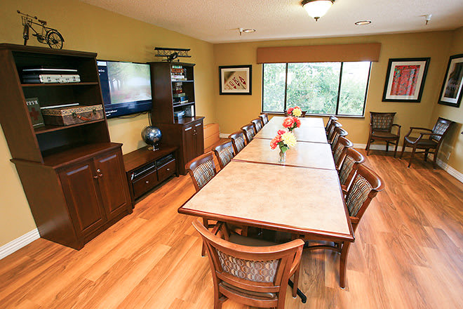 A well-appointed conference room featuring a long meeting table and chairs, with a television and cabinets at one end, and natural light streaming in from large windows.