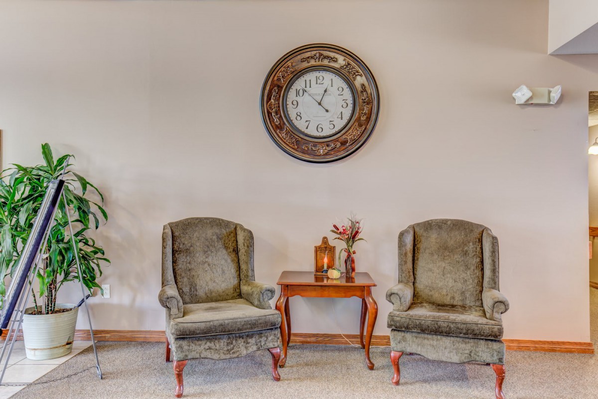 A cozy living room setting with two armchairs, a small wooden table, and a large wall clock.