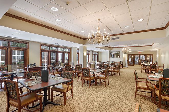 An elegant dining room with multiple tables and chairs, adorned with chandeliers and a carpeted floor.