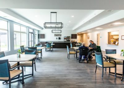 A modern dining area with several tables and chairs, featuring people interacting in a spacious, well-lit setting.