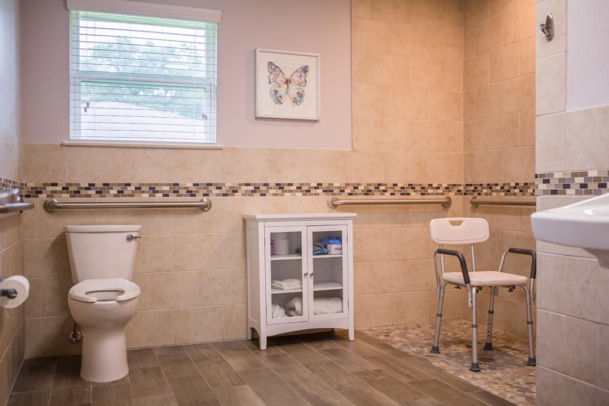 A spacious bathroom with a toilet, shower chair, and storage cabinet adorned with decorative tiles and butterfly artwork.