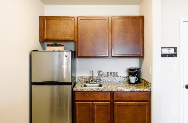 A compact kitchen area featuring wooden cabinets, a stainless steel refrigerator, granite countertops, and a coffee maker.
