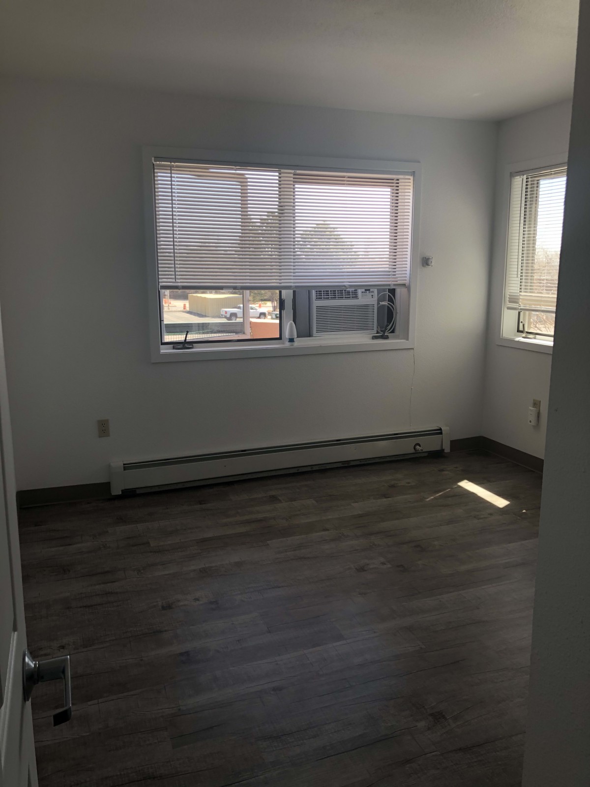 A bright, empty room with hardwood flooring and large windows letting in natural light.