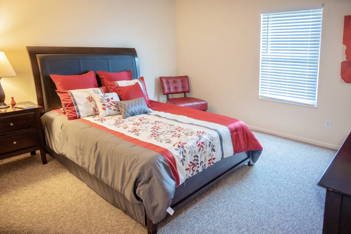 A cozy bedroom with a neatly made bed featuring red and floral accents.