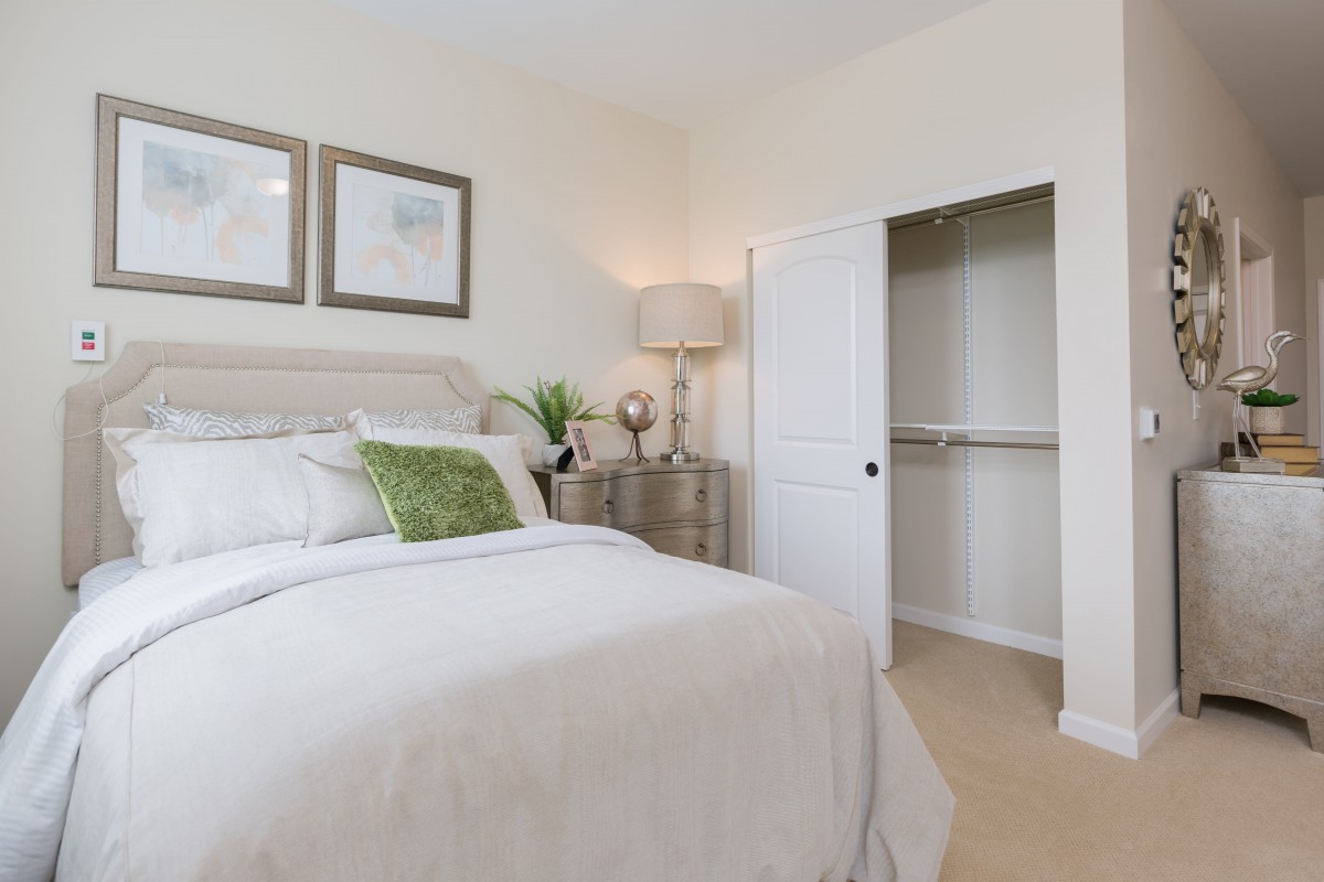 A cozy bedroom with a neatly made bed, decorative pillows, and an open closet.