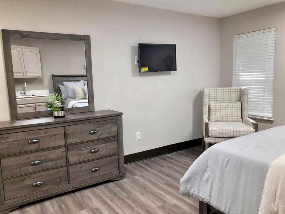 A modern bedroom with a dresser, mirror, and mounted TV.