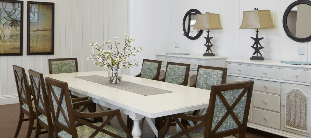 An elegant dining room featuring a white dining table with a flower arrangement and chairs, accompanied by a decorative lamp and mirror.