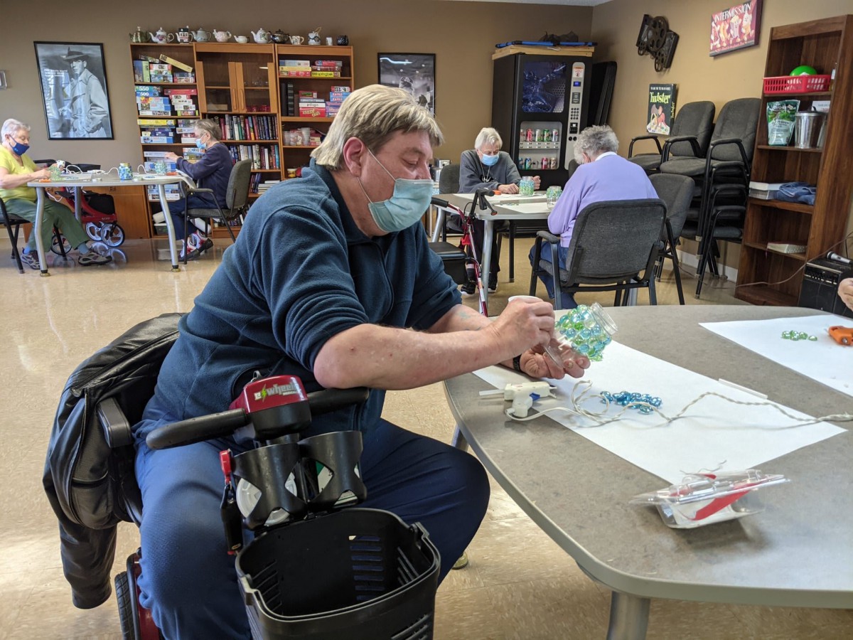 A person wearing a mask engages in a crafting activity indoors with others.