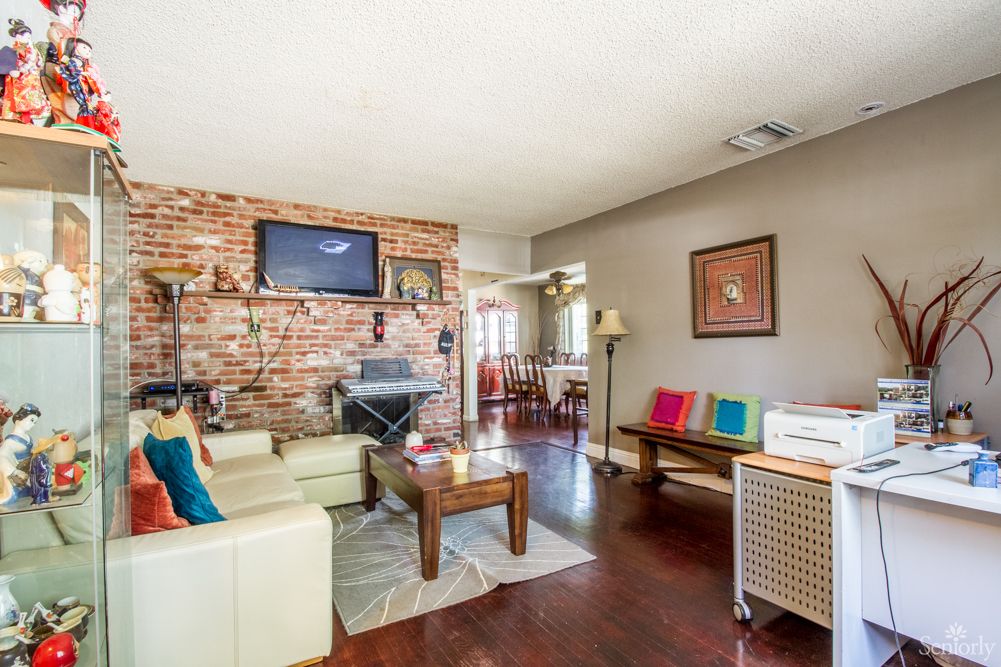 A cozy living room featuring a brick wall with a mounted television, comfortable seating, and colorful decor.