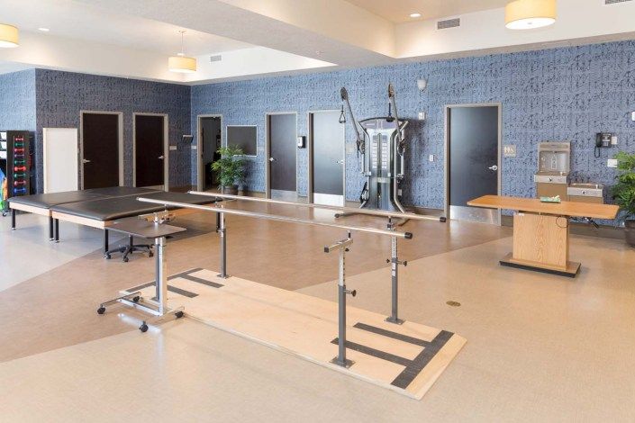 A well-equipped physical therapy room with parallel bars and exercise machines for rehabilitation.