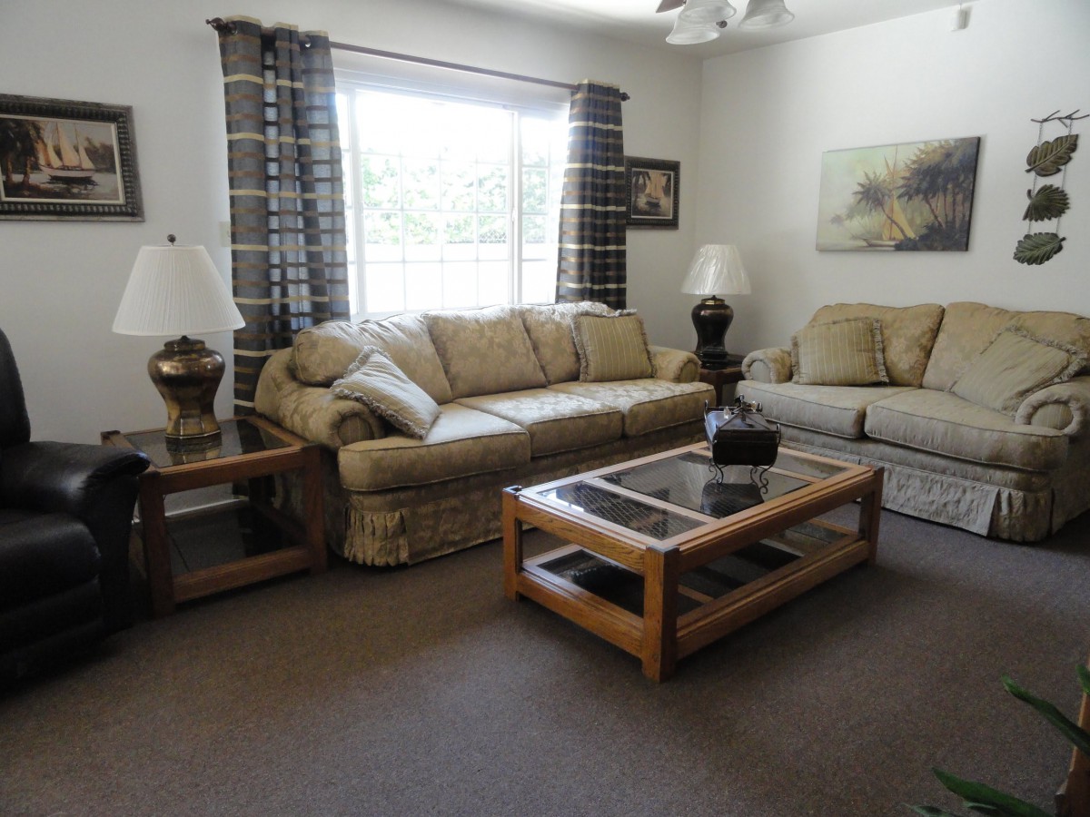 A cozy living room with comfortable sofas, a glass-top coffee table, and decorative lamps by the window.