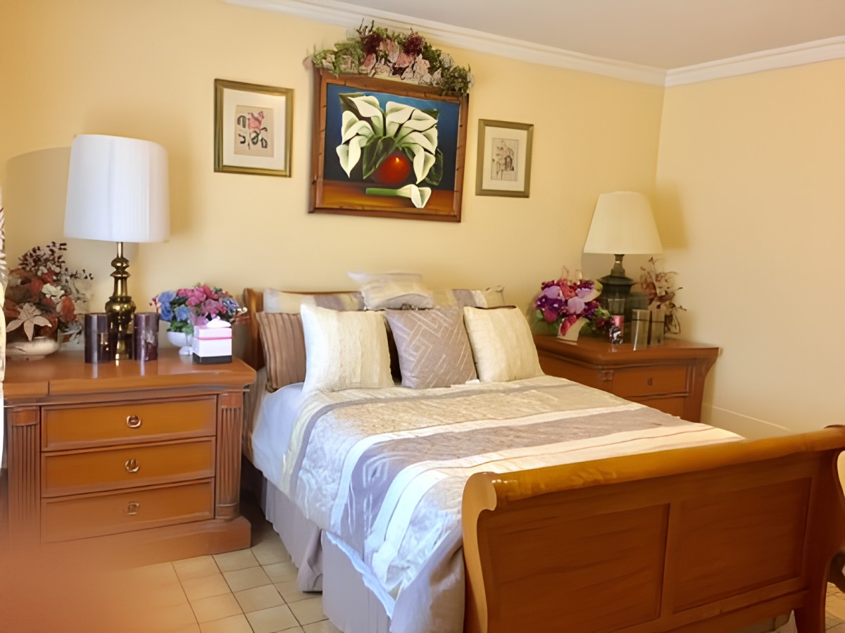 A cozy bedroom with wooden furniture, decorated with flowers and artwork.