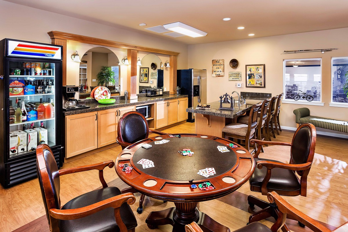 A well-furnished game room featuring a poker table with cards set up, surrounded by comfortable seating and a bar area in the background.