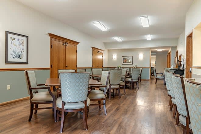 A spacious dining area with multiple tables and chairs, featuring wood flooring and soft lighting.