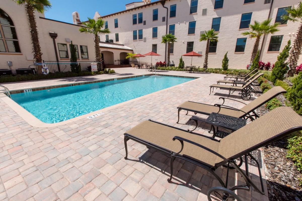 A residential outdoor pool area with sun loungers and palm trees.