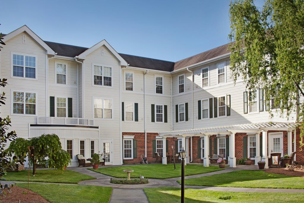 A three-story residential building with a well-maintained garden and lawn in the foreground.