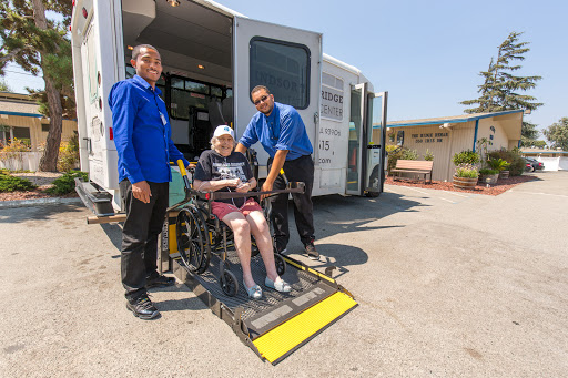 Caregivers assisting a senior in a wheelchair as they prepare for transportation.