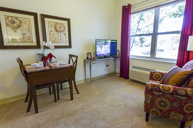 A cozy living room with a dining table, chairs, television, and a window with curtains.