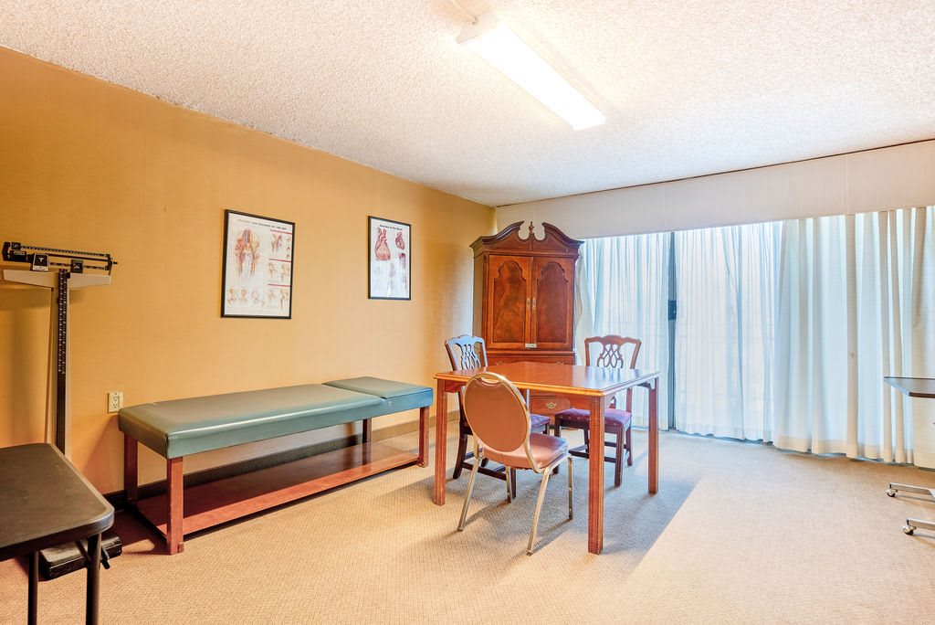 An office space with an examination table, a wooden desk, chairs, and medical posters on the walls.