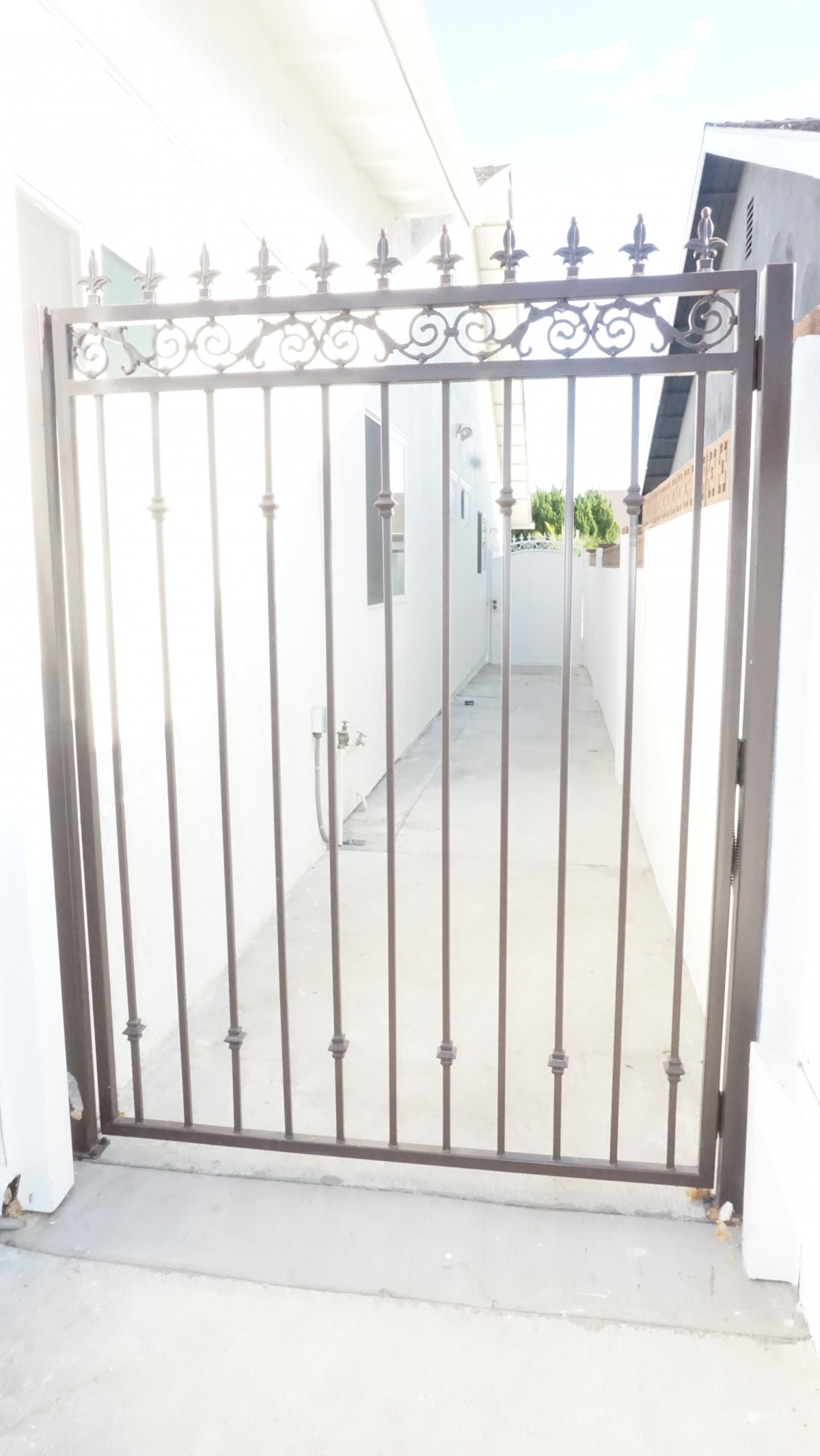 A metal gate providing security to a narrow outdoor pathway.
