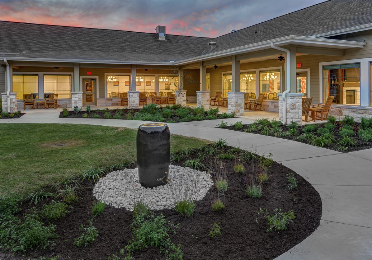 A beautifully landscaped courtyard with a central stone feature, surrounded by a modern building at dusk.