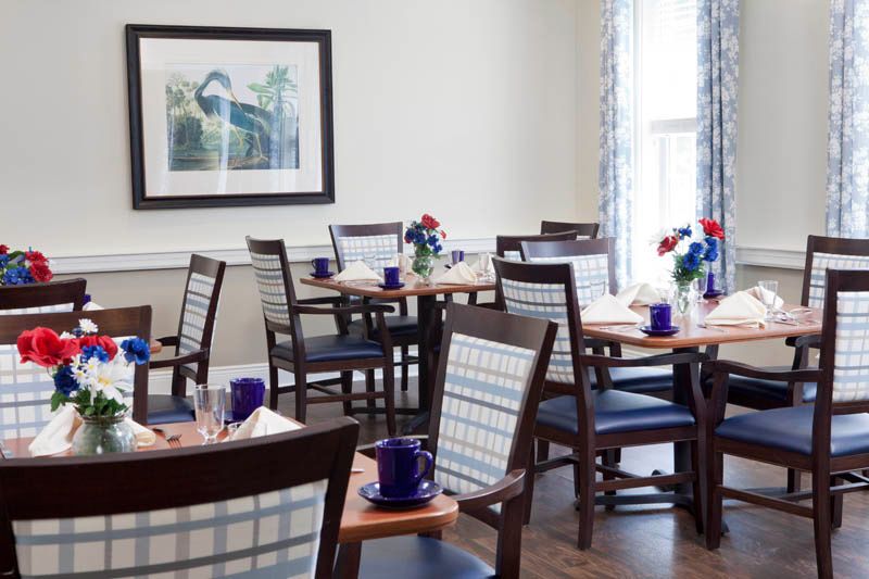A well-arranged dining area with tables and chairs set up for guests, featuring decorative flowers and place settings.
