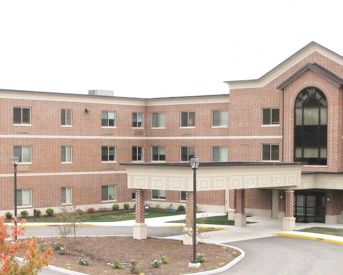 A three-story brick healthcare facility with a covered entrance and surrounding landscaping.