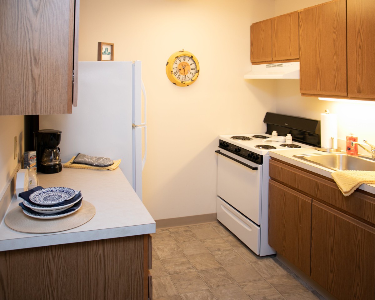 A cozy kitchen featuring wooden cabinets, a stove, refrigerator, and a countertop with plates.