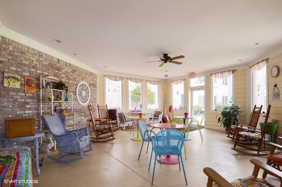 A cozy living room with rocking chairs and colorful furniture, filled with natural light from large windows.