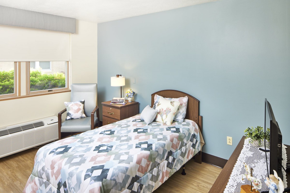 A cozy bedroom with a twin bed, featuring a blue accent wall, nightstand, and armchair.