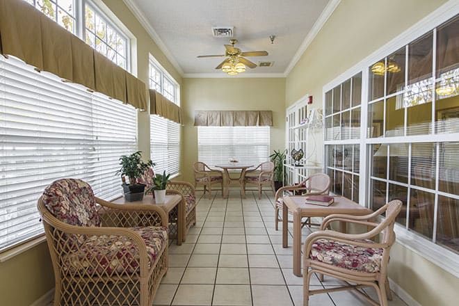 A cozy sunroom filled with natural light, showcasing wicker furniture and potted plants.