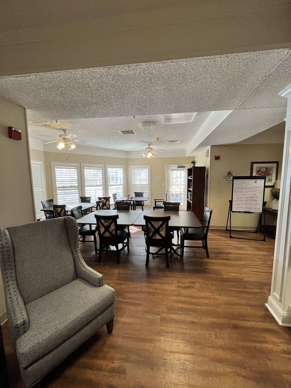 A cozy dining area featuring a large table with chairs, an armchair, and several windows allowing natural light.
