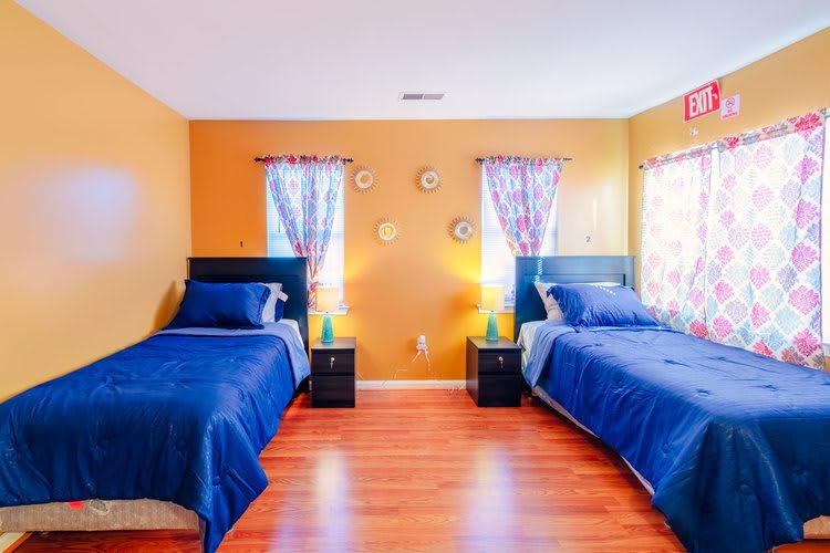 A cozy bedroom with twin beds, vibrant orange walls, and blue bedding.