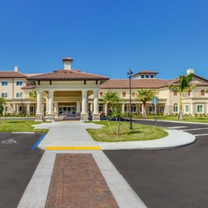 A sunny view of a building entrance with well-maintained landscaping and a circular driveway.