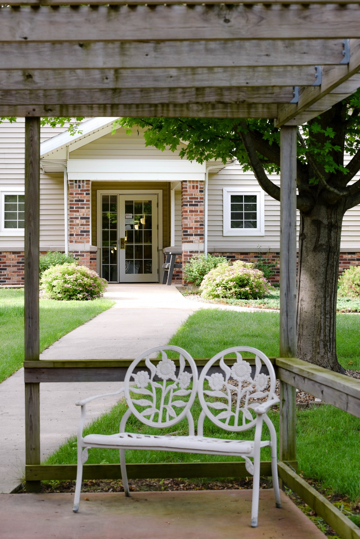 A tranquil garden with a white bench facing a building entrance.