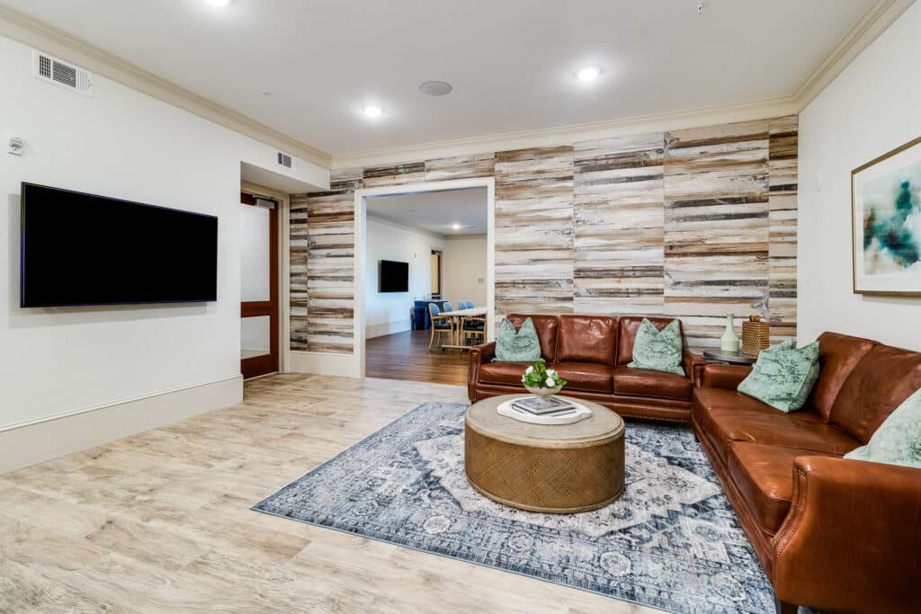A modern living room featuring a leather sectional sofa, decorative rug, and wood accent wall with a TV.