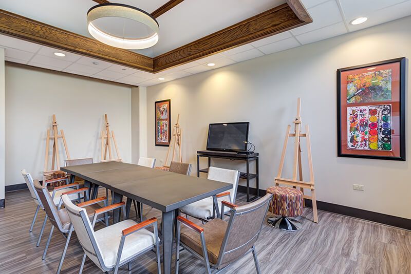 A modern meeting room with a large conference table, chairs, art easels, and a television.