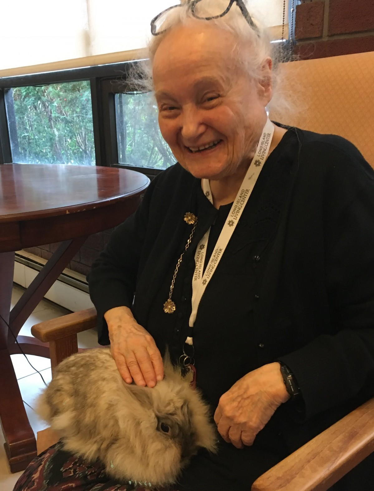 An elderly woman smiling while sitting indoors with a pet on her lap.