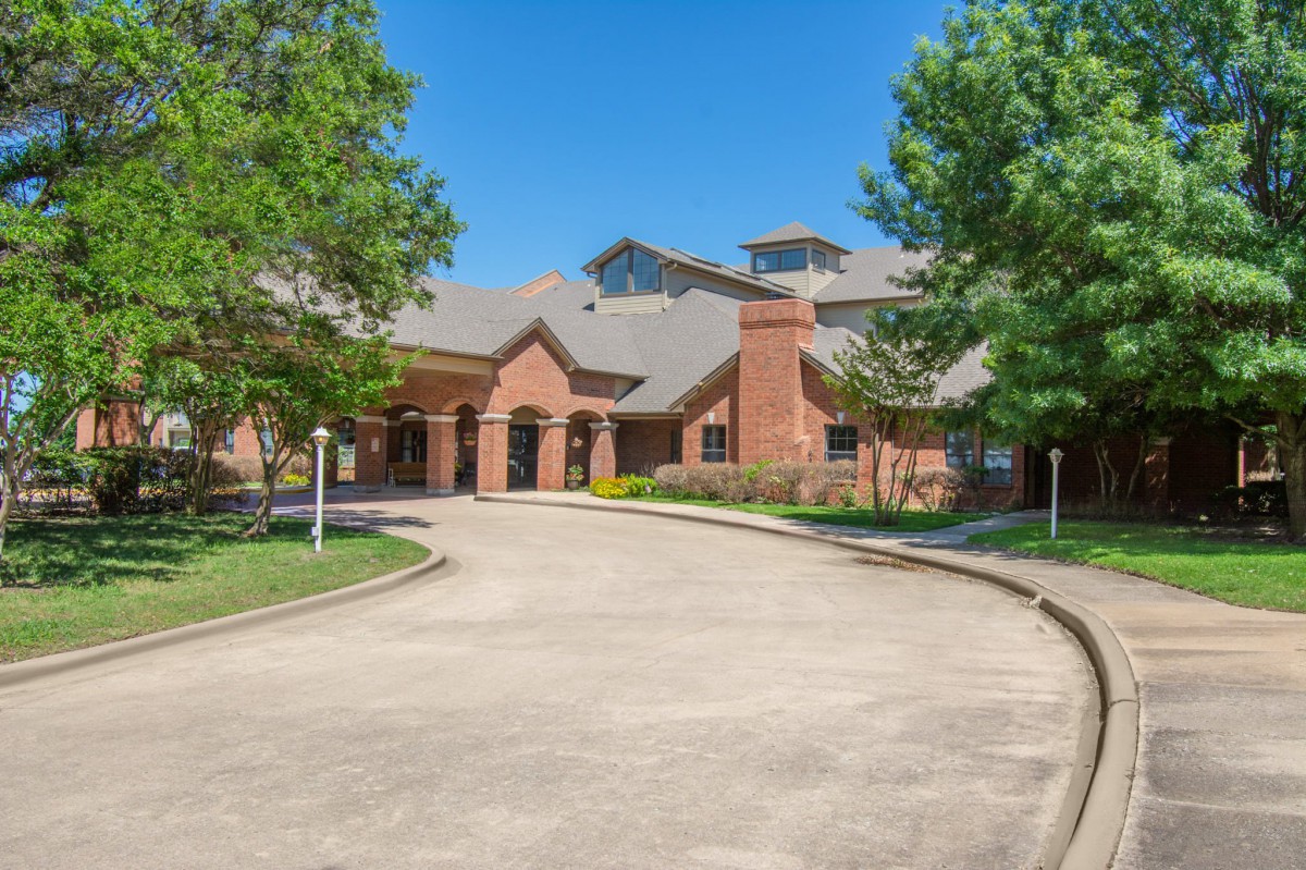 A picturesque brick house with a curved driveway and lush trees surrounding it.