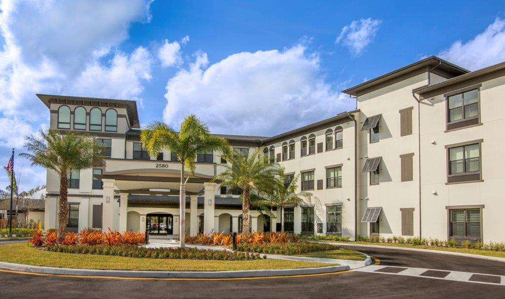 A modern building with palm trees and landscaped surroundings under a partly cloudy sky.