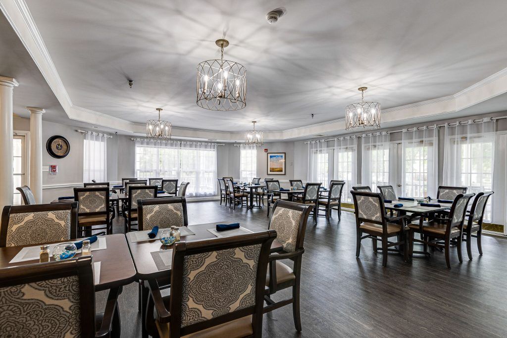 A spacious and elegantly designed dining room with multiple tables and chairs, featuring large windows and decorative chandeliers.