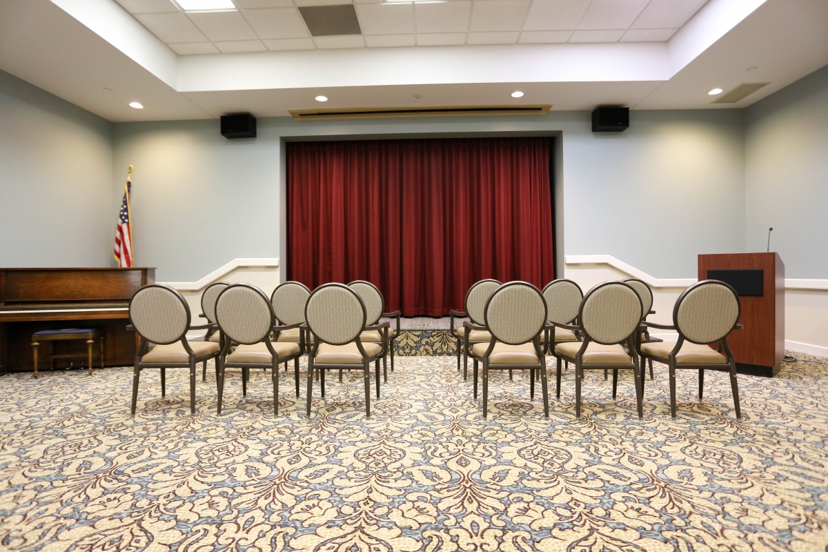 An empty conference room with chairs arranged in a theater setup facing a red curtain.