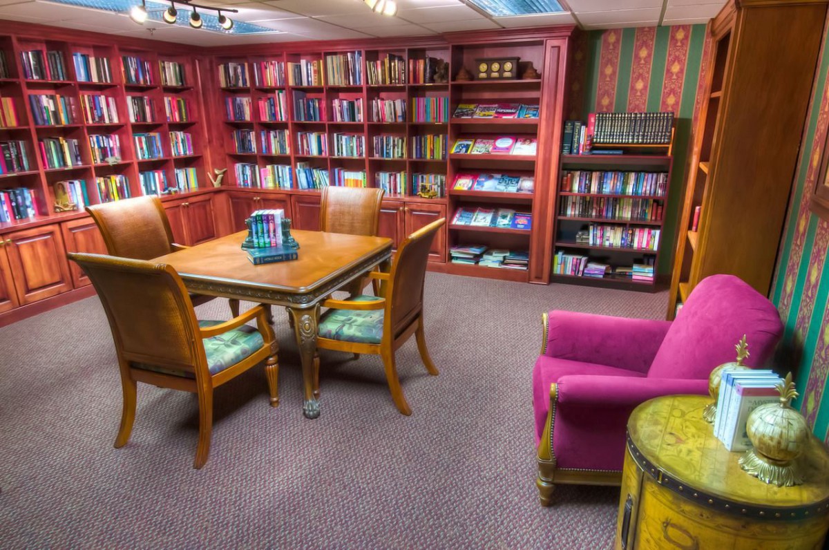 A cozy library reading room with bookshelves, a table, and comfortable chairs.