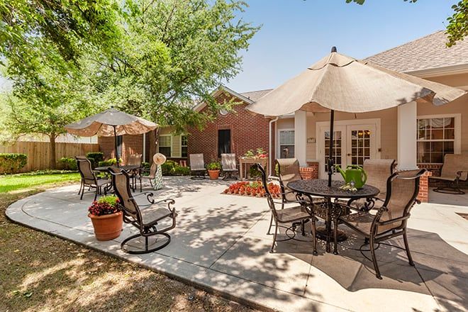 A sunny outdoor patio with tables, chairs, umbrellas, and potted plants.