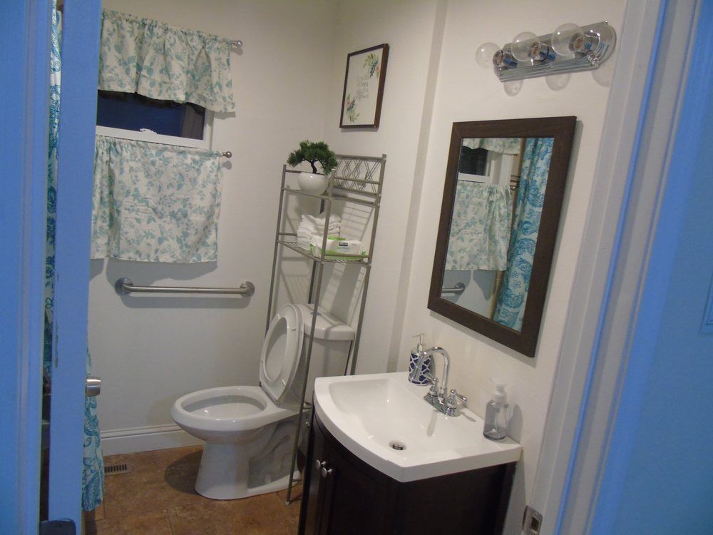 A neatly organized bathroom featuring a toilet, sink, mirror, and shelving unit with decor.