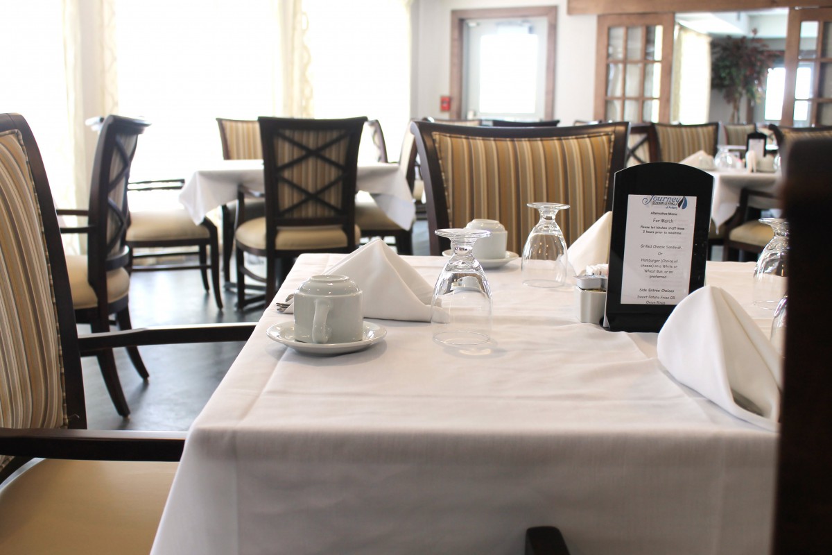 A neatly set dining table in a restaurant, featuring white tablecloths and elegant place settings.