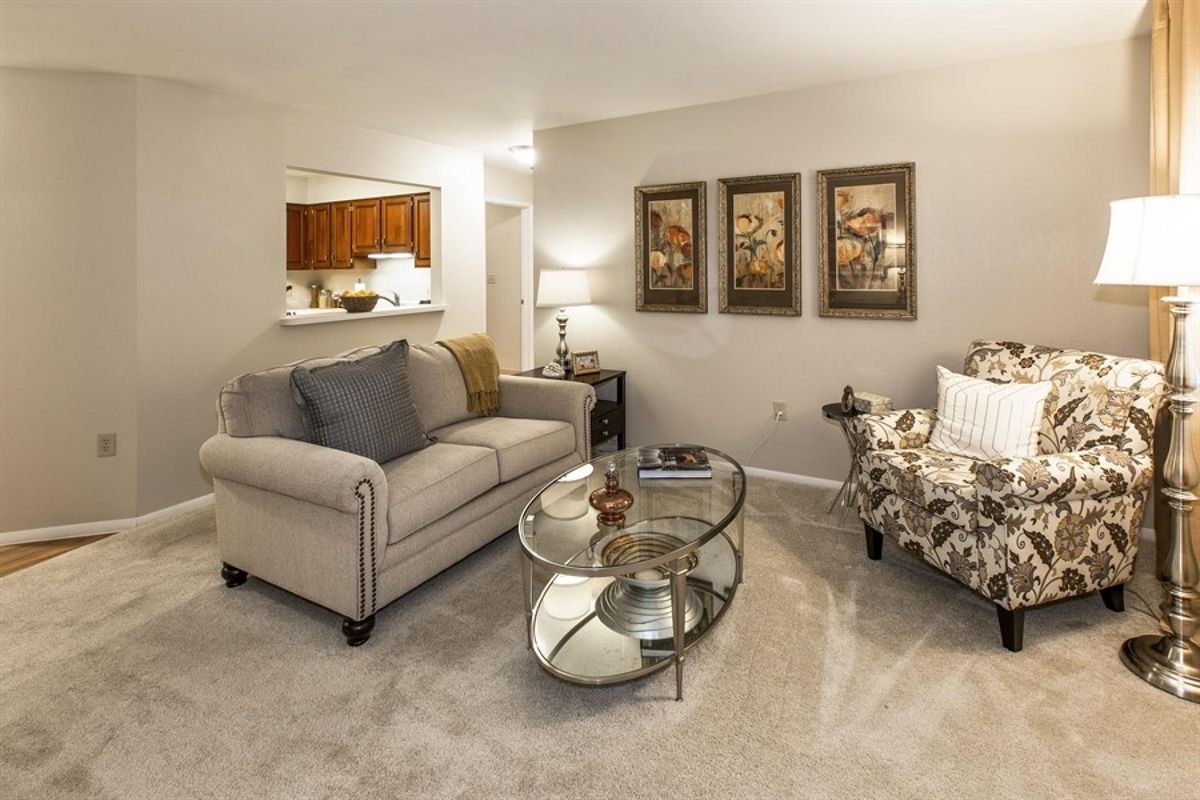 A cozy living room featuring a comfortable sofa, an upholstered chair, a glass coffee table, and decorative artwork on the walls.