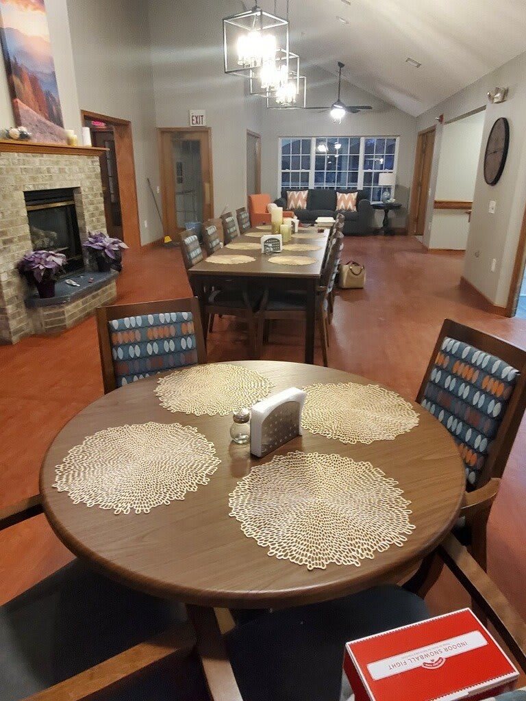 A cozy dining area with neatly arranged tables and chairs, featuring a fireplace in the background.
