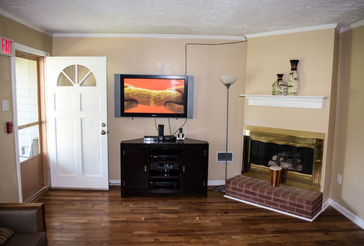 A cozy living room with a mounted television, brick fireplace, and hardwood flooring.
