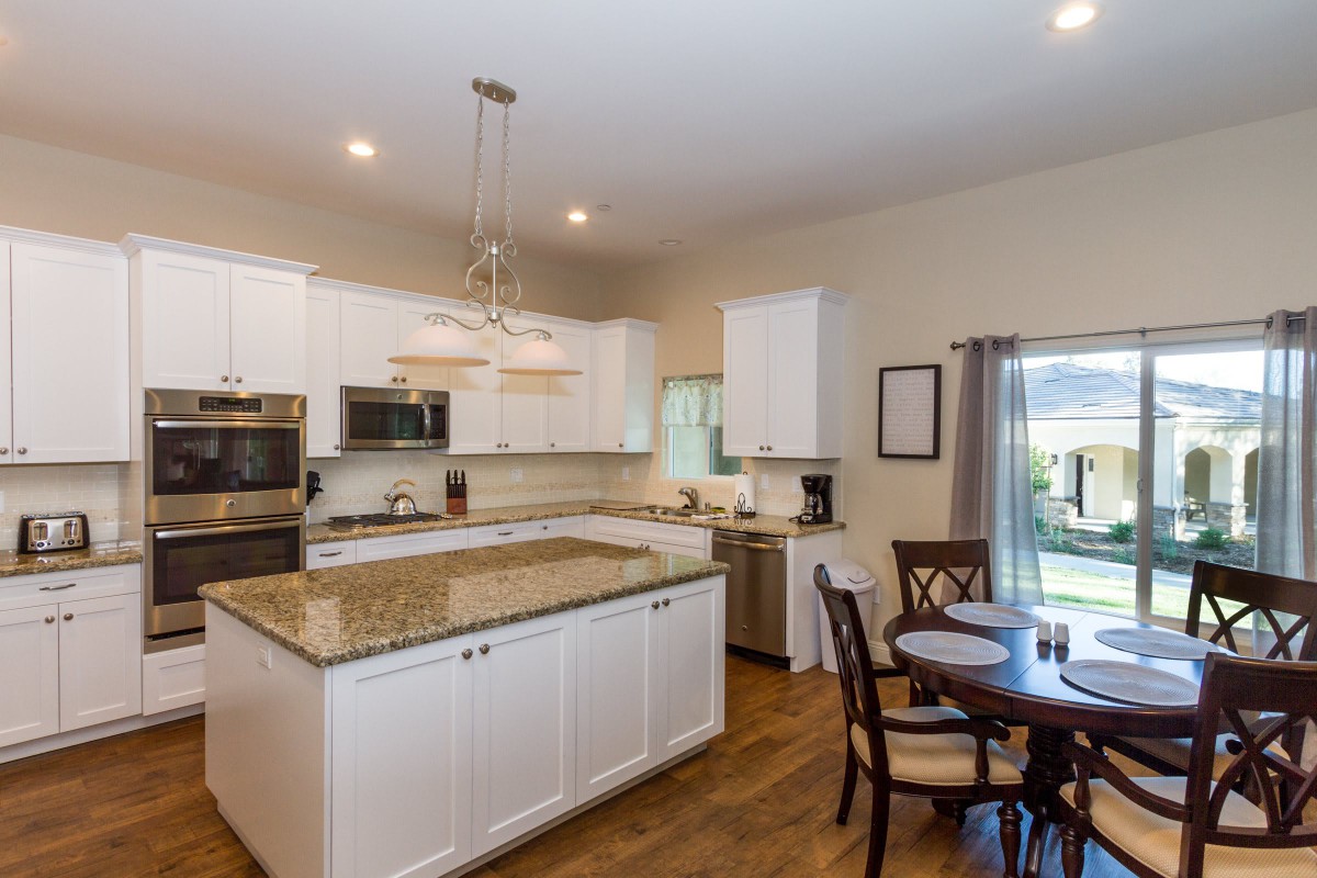 A modern kitchen with white cabinets, granite countertops, and a dining area.